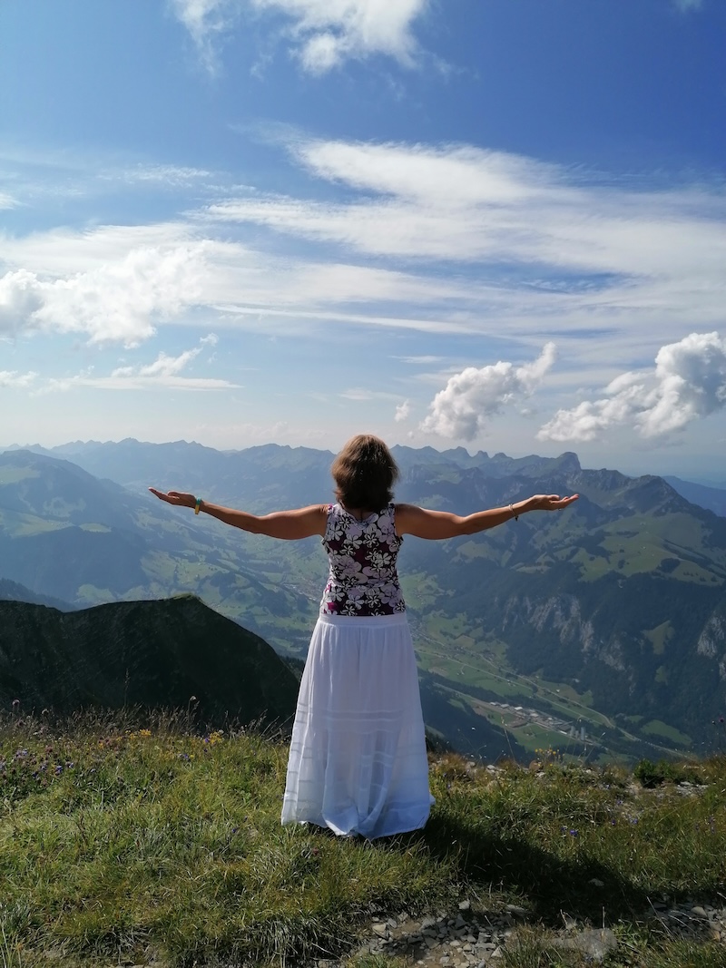 Frau auf einem Berggipfel mit ausgebreiteten Armen